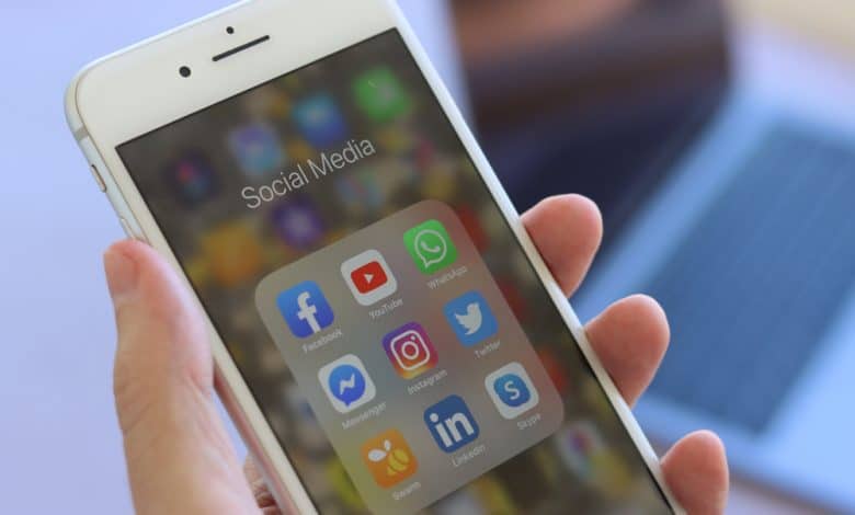 وسائل التواصل الاجتماعي - يد تمسك بهاتف محمول يعرض تطبيقات الوسائل الاجتماعية